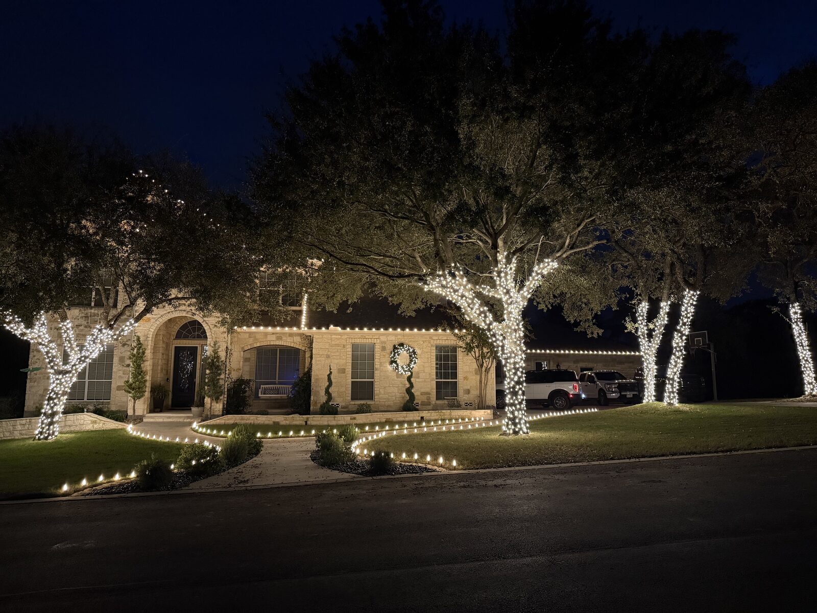 Professionally lit stone home at night — warm white roofline, trees, and walkway lights by Lights & Rescue